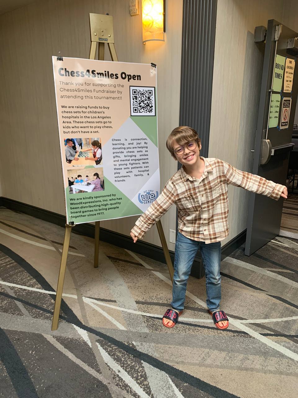 Keith beside a Chess4Smiles fundraiser poster.