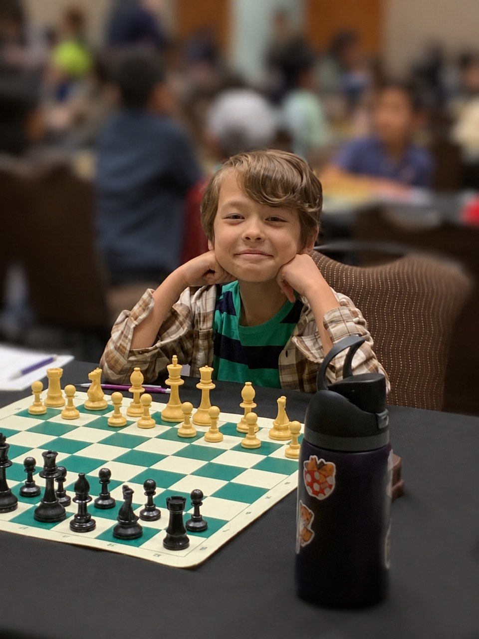 Keith Tokuhara smiling with his chin resting on his hands at a chess tournament.